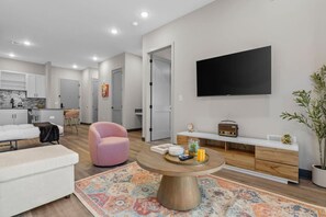 Ein modernes Wohnzimmer mit einer Couch, einem rosa Sessel, einem Couchtisch und einem an der Wand befestigten Fernseher.