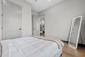 A bedroom with a bed, a wardrobe, a mirror, and a door leading to another room.
