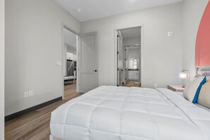 A bedroom with a large bed, a nightstand with a lamp, and a door leading to a bathroom.