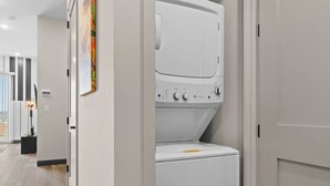 Une buanderie équipée d’un lave-linge et d’un sèche-linge superposés, d’une porte avec une poignée et d’un luminaire fixé au mur.