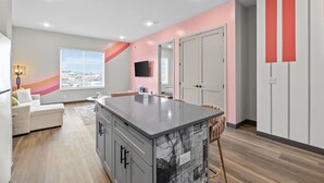 Une cuisine moderne avec un îlot central, des armoires blanches et un mur d’accent rose.