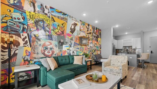 Ein modernes Wohnzimmer mit einem farbenfrohen Wandgemälde, einem grünen Sofa, einem Couchtisch und einer Küchenzeile im Hintergrund.