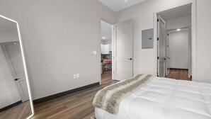 Een moderne slaapkamer met een groot bed, een spiegel en uitzicht op de woonkamer.