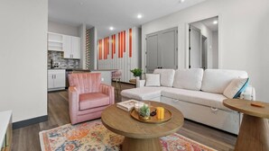 Een moderne woonkamer met een bank, een roze fauteuil, een salontafel en een kamerkleed met een patroon.