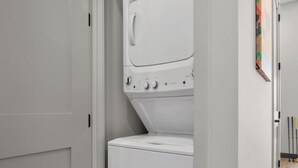 A white washing machine in a laundry room with a door and a wall-mounted artwork. - 1BR Spacious Apt Near Nashville’s Iconic Broadway (Nashville)