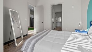 A modern bedroom with a large bed, a bedside table, and a view of a kitchen and living area through an open door. - 1BR Spacious Apt Near Nashville’s Iconic Broadway (Nashville)