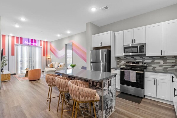 A modern kitchen with white cabinets, stainless steel appliances, and a central island with bar stools. - Spacious 1BR for 4, Free WiFi | 8 Min to Broadway (Nashville)