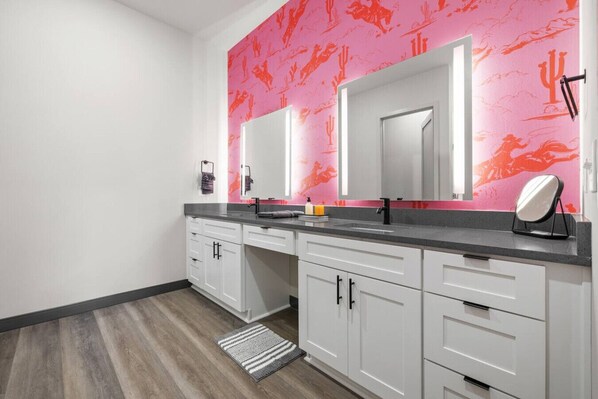 Een moderne badkamer met witte kastjes, een grijze aanrecht en een roze muur met een cactustextuur.