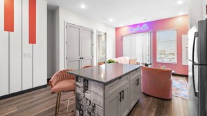 A modern kitchen with a central island, pink chairs, and a neon sign. - Chic 2BR Getaway in Downtown Nashville! (Nashville)