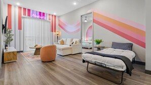 Ein modernes Schlafzimmer mit einem Bett, einem Sofa, einem Sessel, einem kleinen Tisch und einem Spiegel.