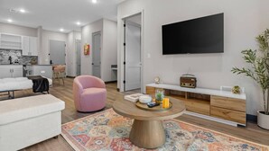 Ein modernes Wohnzimmer mit einer Couch, einem rosa Sessel, einem Couchtisch und einem an der Wand befestigten Fernseher.