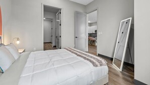 A bedroom with a large bed, a bedside table with a lamp, and a full-length mirror. - 2BR Apt - Parking & 8 Min to Broadway, Sleeps 6! (Nashville)