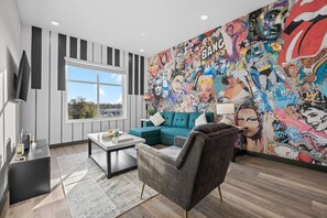 A modern living room with a teal sofa, a grey armchair, and a coffee table. A large comic book-style mural adorns the wall.