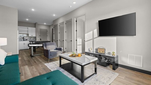 A modern living room with a sofa, a coffee table, a TV, and a kitchen in the background. - 1BR Getaway – Perfect Location for Music Lovers! (Nashville)