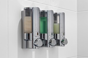 A wall-mounted dispenser with four compartments labeled conditioner, shampoo, body wash, and soap.