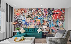 Un salon agrémenté d’une fresque murale colorée de style pop art, d’un canapé turquoise et d’un fauteuil gris.