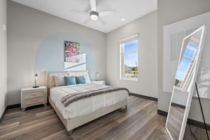 Une chambre à coucher comprenant un lit, deux tables de chevet, un ventilateur de plafond, une fenêtre et un grand miroir.