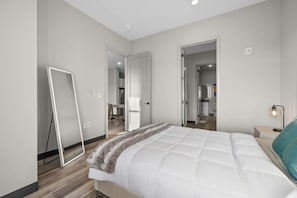 Une chambre à coucher moderne avec un grand lit, une table de chevet avec une lampe et un miroir au mur.