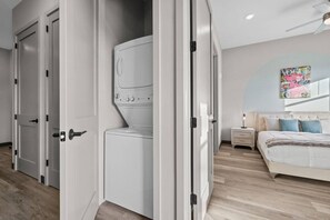 Une chambre moderne avec un grand lit, une table de chevet, une œuvre d’art accrochée au mur et un appareil lave-linge-sèche-linge intégré.