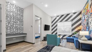 Une chambre d’hôtel moderne avec un grand lit, un coin salon comprenant un canapé et un fauteuil bleus, un téléviseur fixé au mur et un papier peint à motifs sur un des murs.