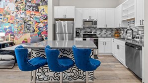 Une cuisine moderne avec des armoires blanches, des appareils en acier inoxydable et une fresque colorée sur le mur.