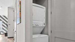 A laundry room with a stacked washer and dryer, a striped wall, and a door leading to another room.