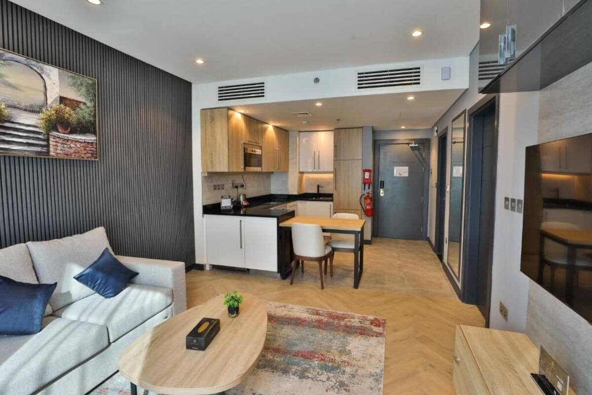 A modern kitchen with white cabinets, a dining area with a wooden table and chairs, and a living area with a sofa and coffee table.