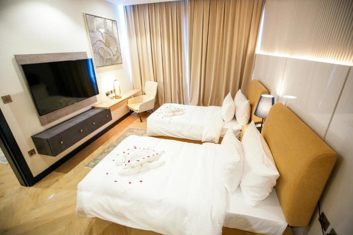 A hotel room with two beds, a TV, a desk, and a large window with curtains.
