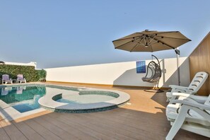 A rooftop pool area with a hot tub, lounge chairs, and a ceiling fan.