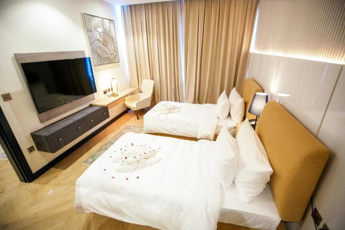 A hotel room with two beds, a TV, a desk, and a large window with curtains.