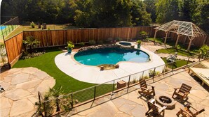 Ein Garten mit Schwimmbad, Stein-Terrasse, Holzdeck und einer Sitzgelegenheit im Freien.
