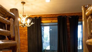 Ein Holzinterieur mit einem Esstisch, Stühlen, einer Kandelaber und einem großen Fenster mit Vorhängen.