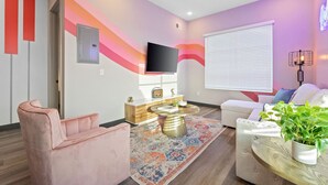 Una sala de estar moderna con un sillón rosa, un sofá blanco, una mesa de centro y un televisor montado en la pared.