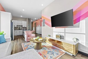 Ein modernes Wohnzimmer mit einem an der Wand befestigten Flachbildfernseher, einem pinken Sessel, einem runden Couchtisch und einer Holzkommode.
