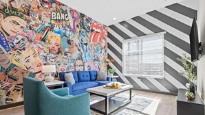 A living room with a vibrant comic-style mural, a blue sofa, a coffee table, and a modern staircase with black and white stripes. - Hip 1BR Hideaway - Quick Drive to Downtown Fun! (Nashville)