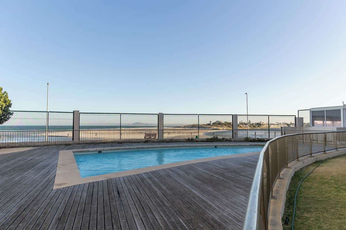 Um deck de madeira com piscina, com vista para uma praia e o oceano.