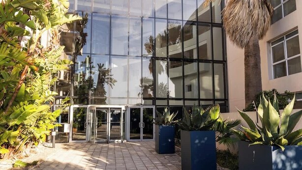 A modern building with a glass facade, a paved entrance area, and potted plants. - Holiday Apartment, Lagoon Beach (Cape Town)
