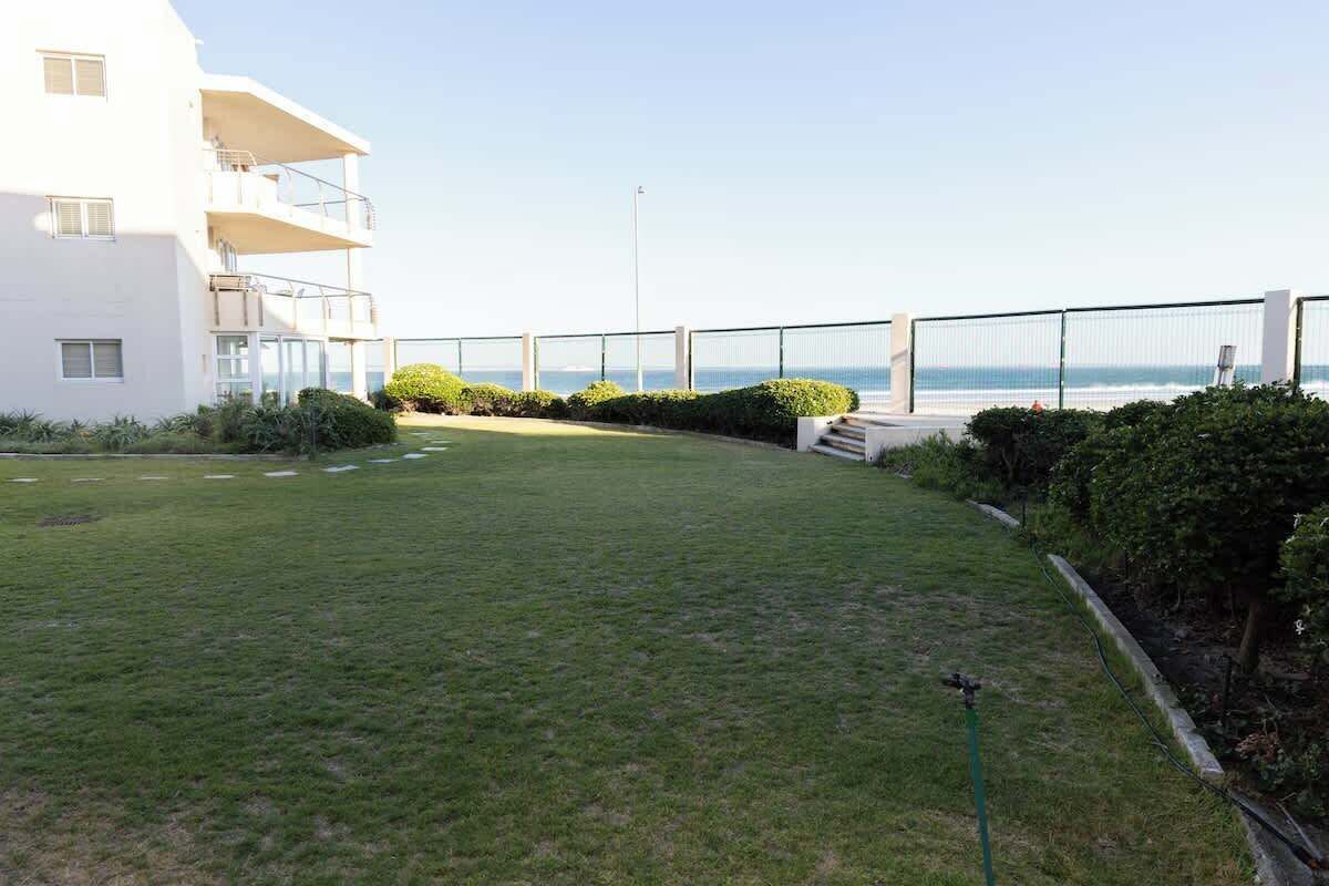 A grassy courtyard with a white building, a balcony, and a view of the sea.