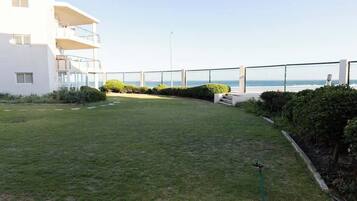 A grassy courtyard with a white building, a balcony, and a view of the sea.