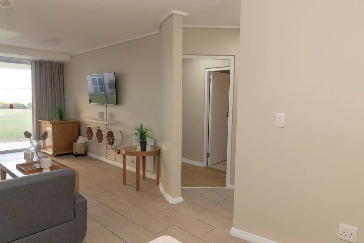 A modern living room with a flat-screen TV, a sofa, a coffee table, and a dining area with a small table and chairs.