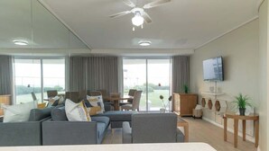 A modern living room with a sofa set, a dining table, and a television on the wall. - Holiday Apartment, Lagoon Beach (Cape Town)