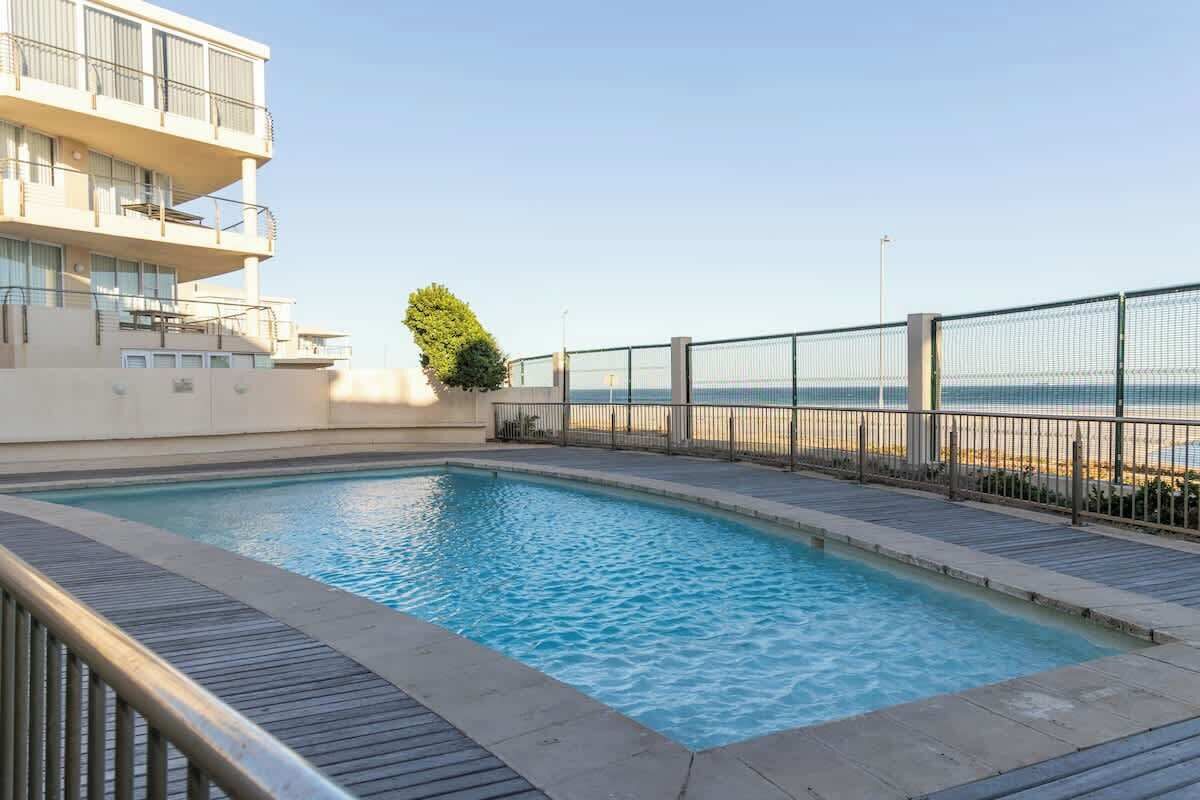 A swimming pool with a view of the sea, a building with balconies, and a fence.