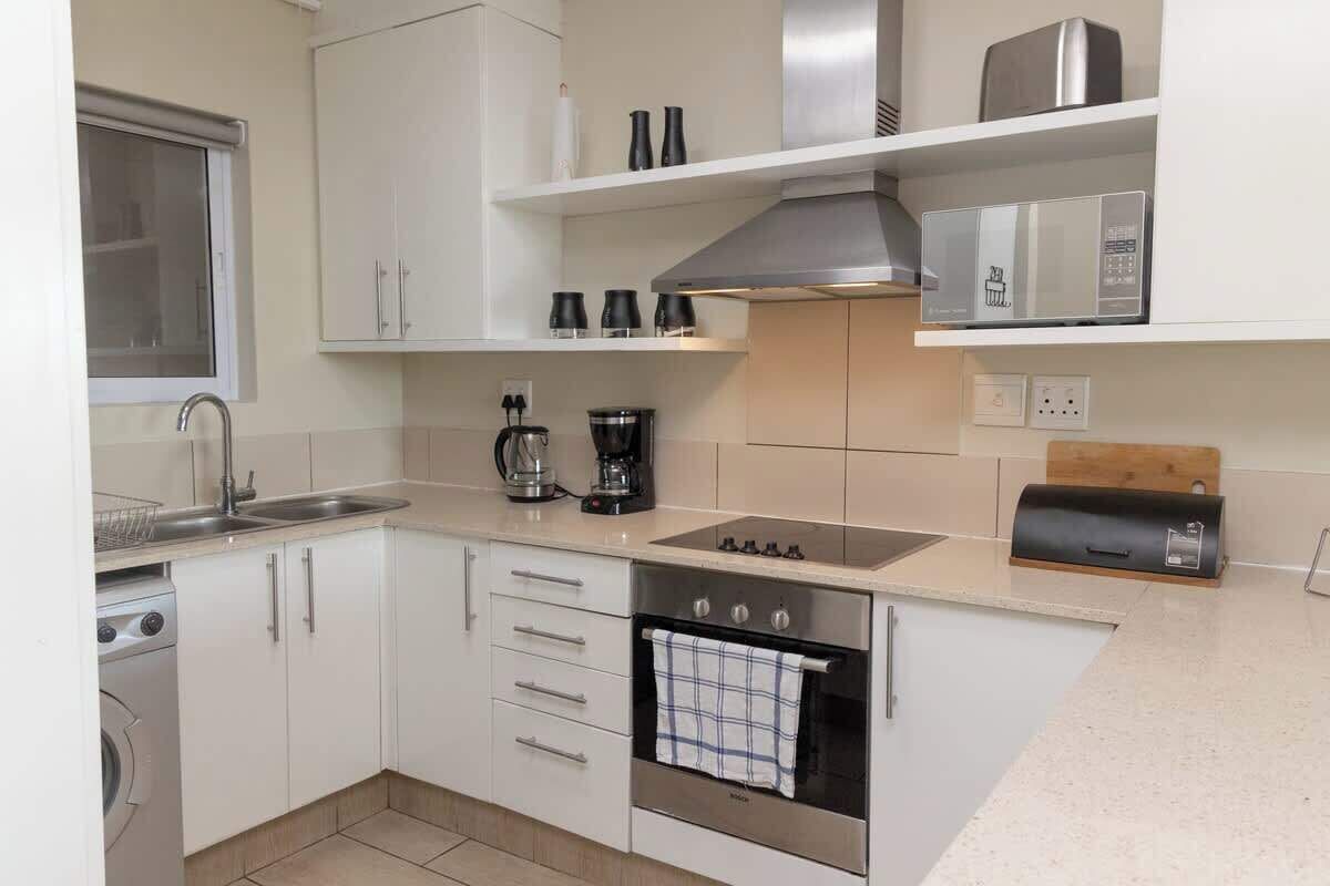 A modern kitchen with white cabinets, a stainless steel range hood, a built-in oven, and a coffee maker.