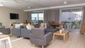 A modern living room with a sectional sofa, a coffee table, and a TV mounted on the wall. - Holiday Apartment, Lagoon Beach (Cape Town)