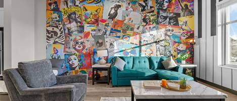 Un soggiorno moderno con un murale colorato, un divano verde acqua e un tavolino da caffè minimalista.