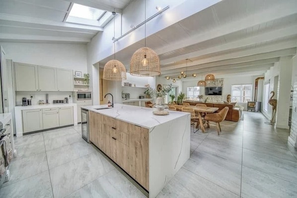 A spacious kitchen with a large island, modern appliances, and a dining area with a high ceiling and pendant lighting.