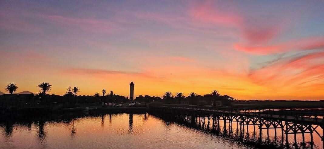 Un coucher de soleil sur une étendue d’eau, avec une jetée et une tour visibles au loin.