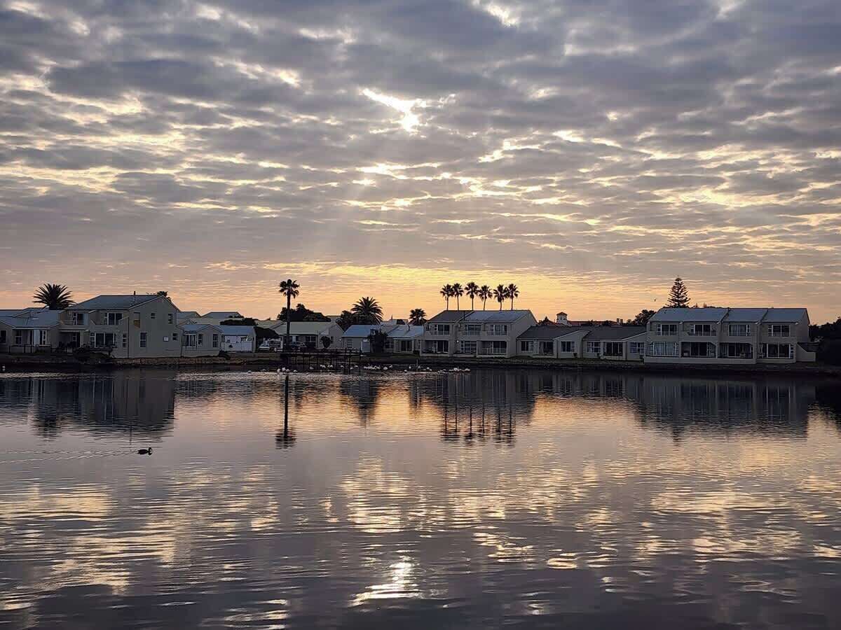 A waterfront property with reflective water, houses, and palm trees against a sunset sky.