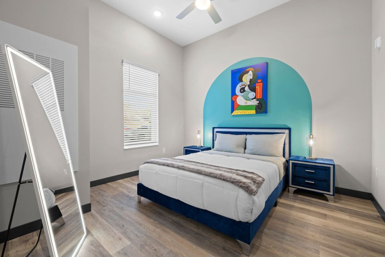 A modern bedroom with a bed, two bedside tables, a ceiling fan, and a large window with blinds.