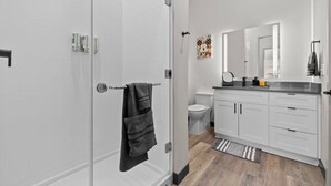 A modern bathroom with white tiles, a glass shower enclosure, a toilet, and a sink with a mirror.